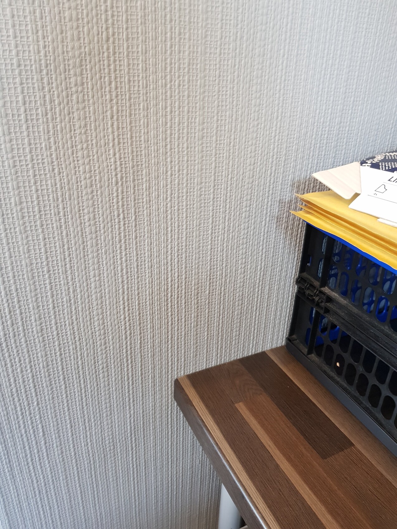 Ecke eines Schreibtischs aus Holz, schwarze Kunststoffkiste mit gelben Ordnern und Papieren darauf.