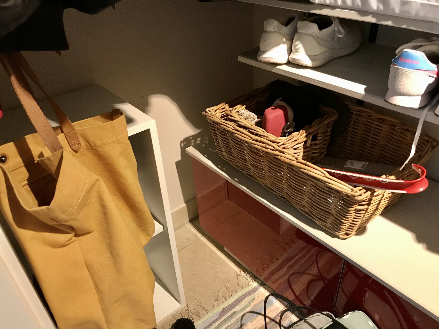 Blick in einen Flurschrank: braune Tasche hängt links, weiße Sneaker oben, Korb mit Gegenständen.
