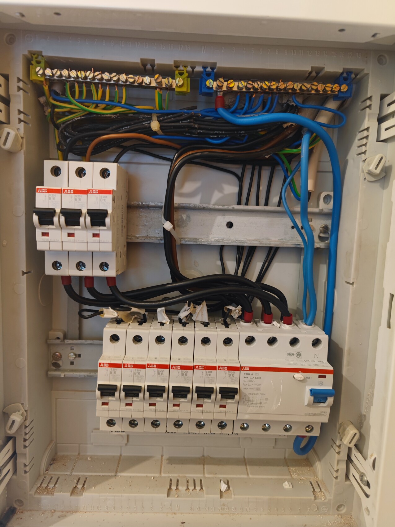 Elektrischer Verteilerkasten mit mehreren Sicherungsautomaten, Kabeln und Montageschienen.