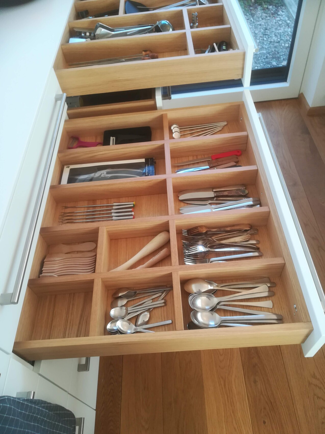 Offene Holzschublade mit Besteck-Organizer; Messer, Gabeln und Löffel sortiert.