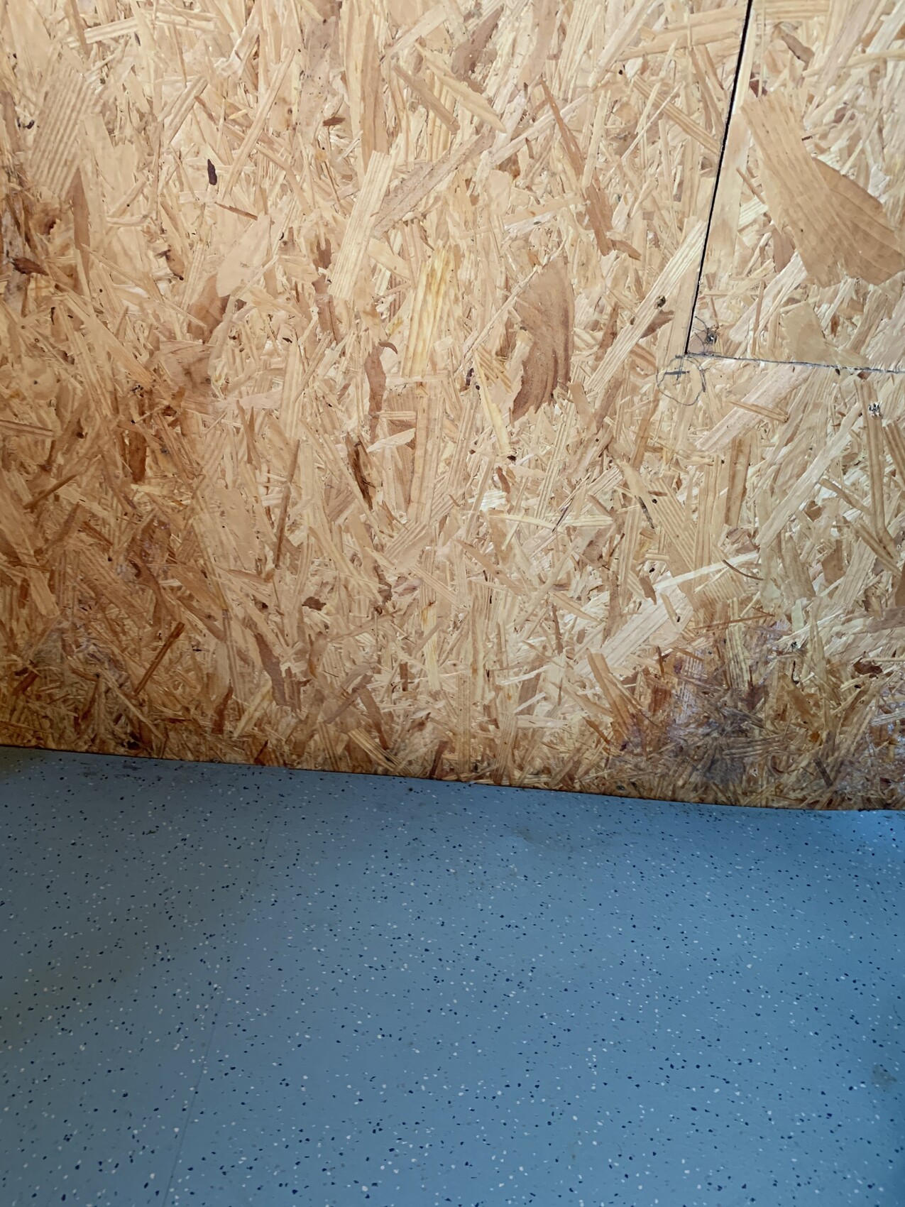 Innenraum einer Werkstatt mit OSB-Wandverkleidung und blauem Boden mit weißen Sprenkeln.
