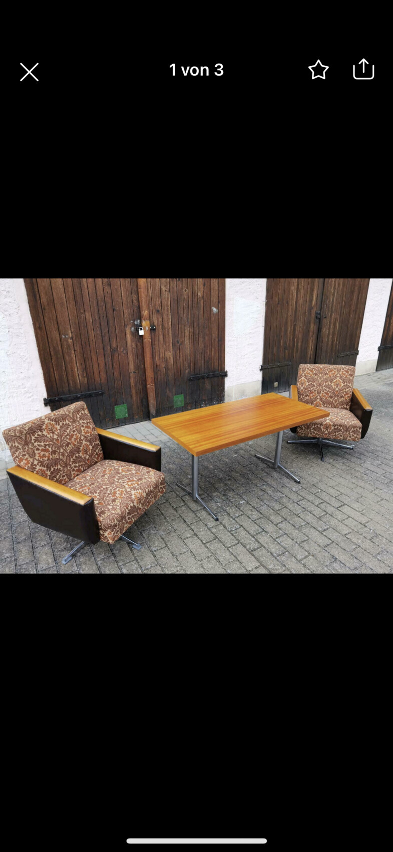 Zwei gepolsterte Sessel mit braunem Muster stehen links und rechts eines Holztisches vor Holztüren.