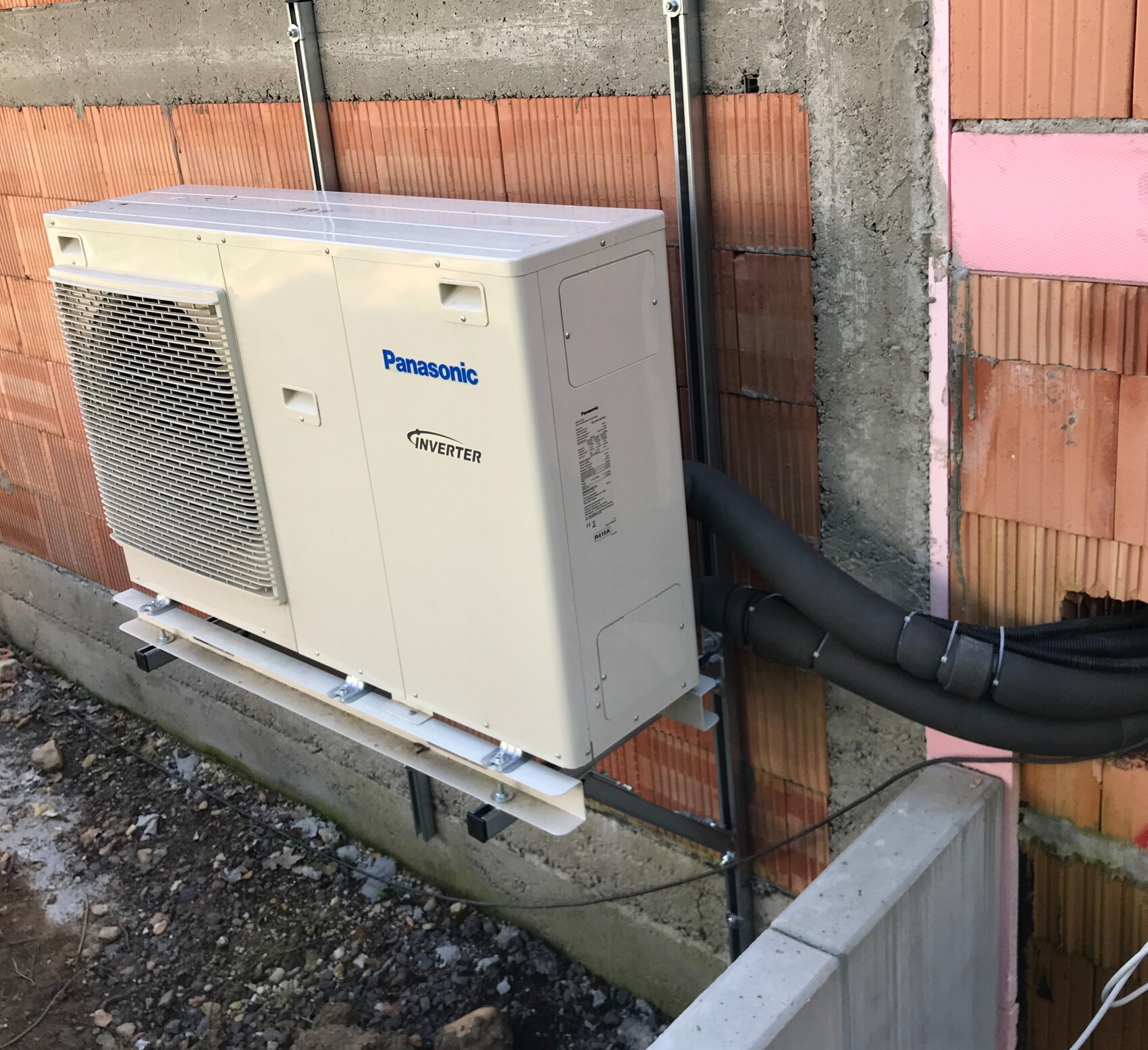 Außen-Klimagerät Panasonic Inverter vor Ziegelwand; schwarze isolierte Rohre sichtbar.