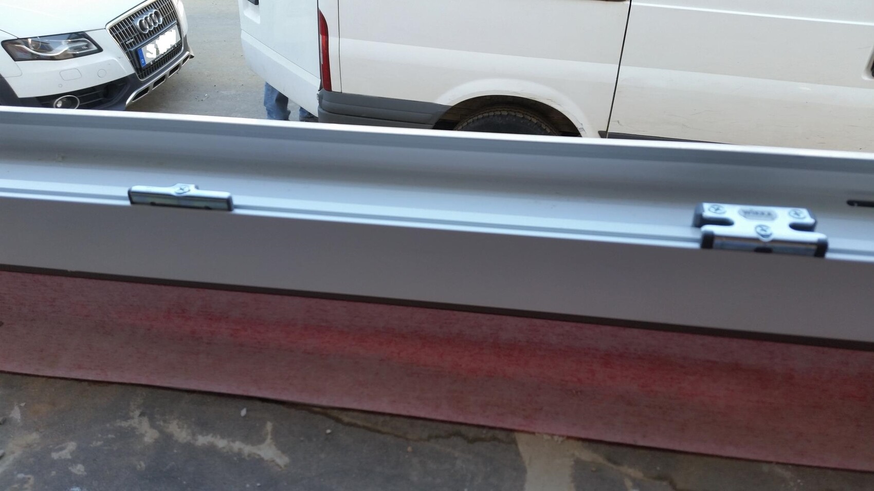 Blick durch Fenster auf weiße Transporter-Van-Seite mit Radkasten, daneben PKW