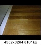 Nahaufnahme eines Holzbodens mit Parkettplatten und heller Sockelleiste im Innenraum.