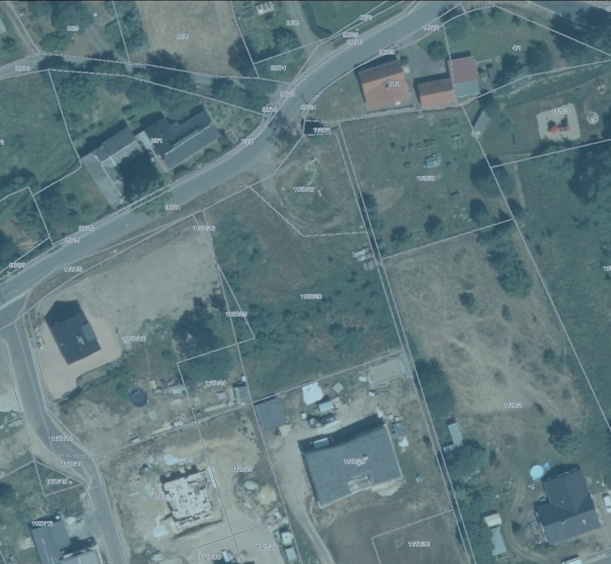 Luftaufnahme einer Straße mit Grundstücksparzellen und Gebäuden.