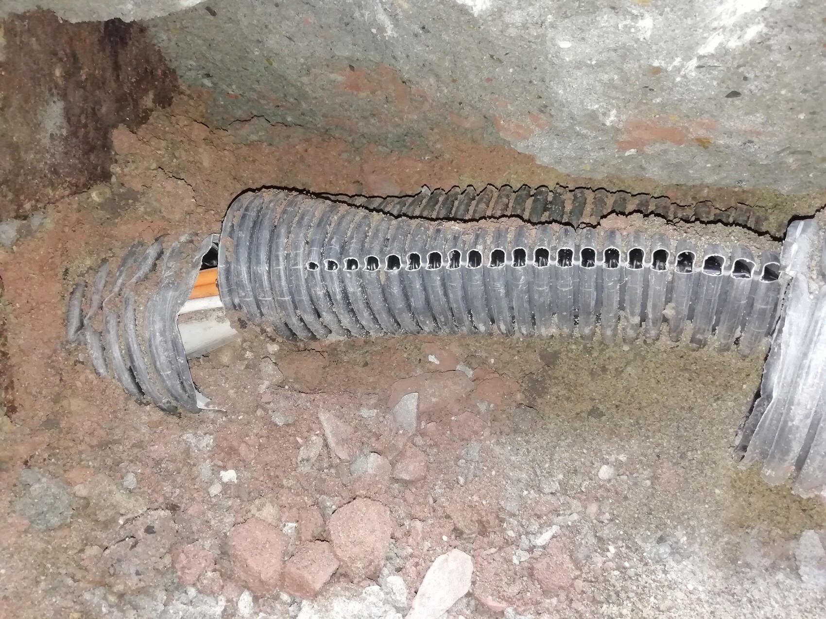 Perforierte Drainageleitung aus Kunststoff im Boden, von Erde bedeckt.