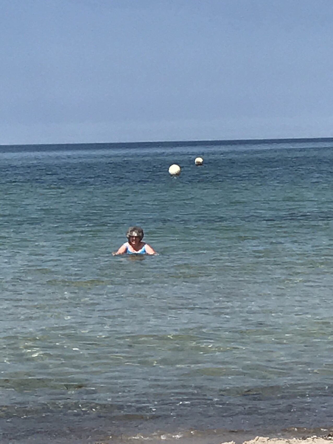 Frau schwimmt im flachen, türkisblauen Meer nahe dem Strand; zwei weiße Bojen treiben vor ihr.