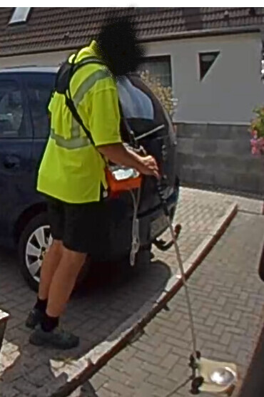 Eine Person in leuchtender Warnweste schiebt eine Person im Rollstuhl auf dem Gehweg.