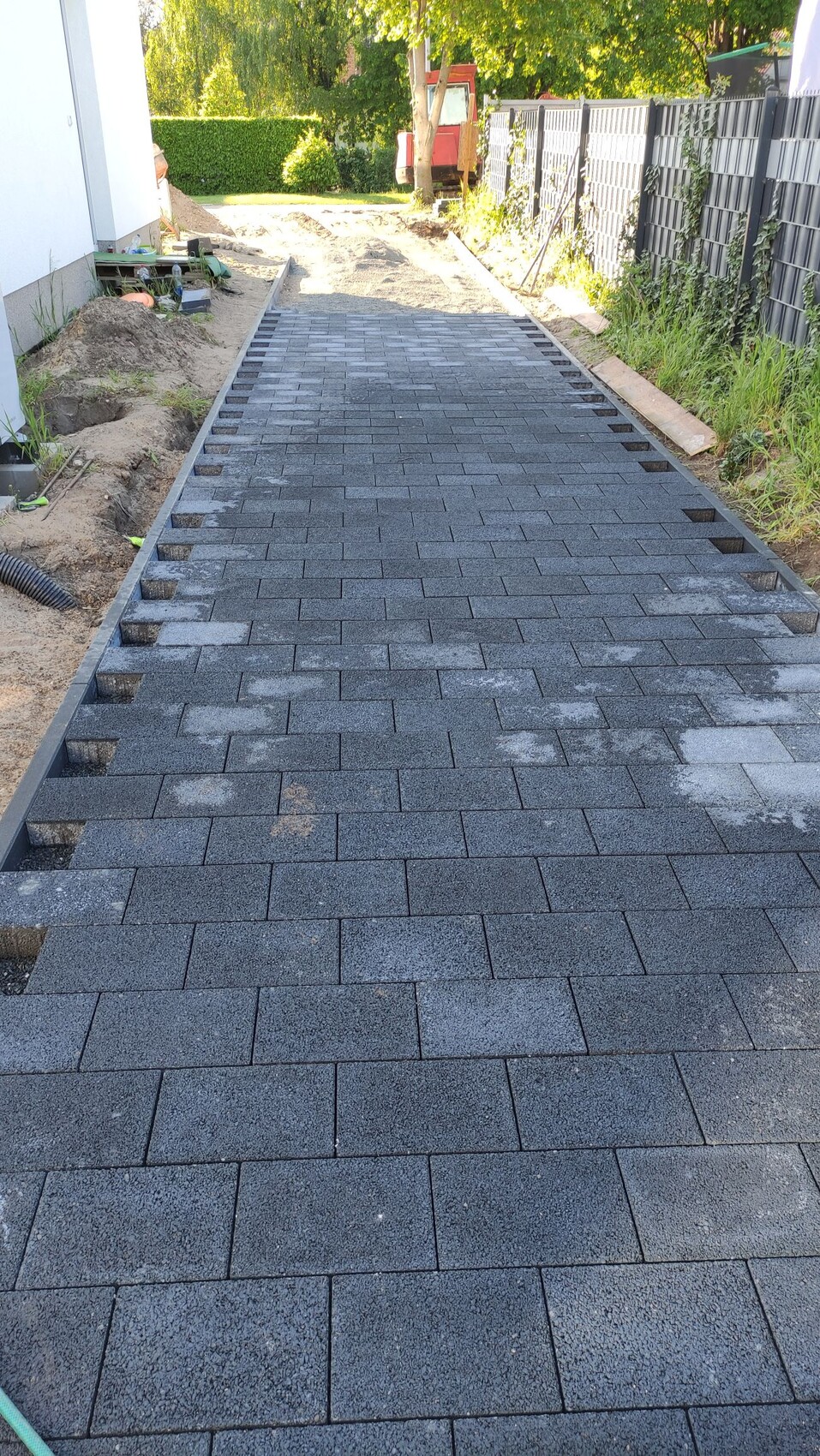 Neu gepflasterte graue Betonstein-Zufahrt mit Randsteinen auf einer Baustelle
