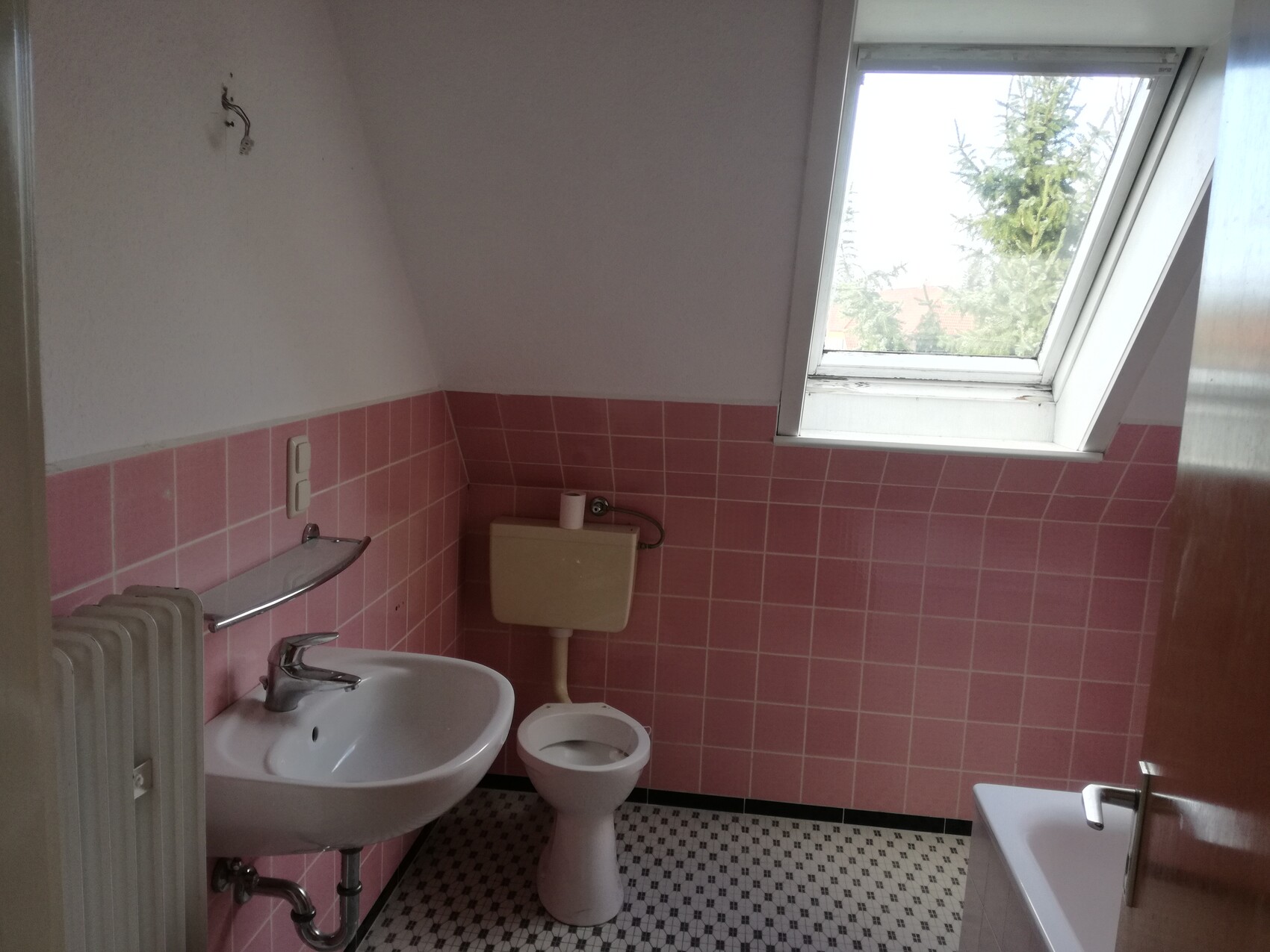 Kleines Badezimmer mit rosa Fliesen, weißem Waschbecken, Toilette und Dachfenster.