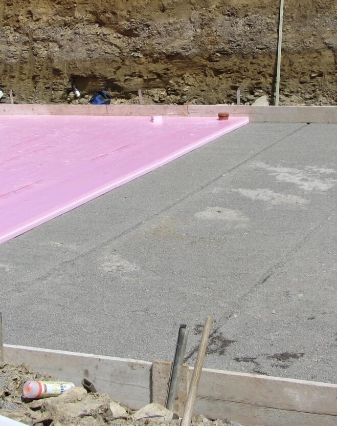 Baustelle mit pinken Dämmplatten auf Fundamentplatte und Erdarbeiten sichtbar