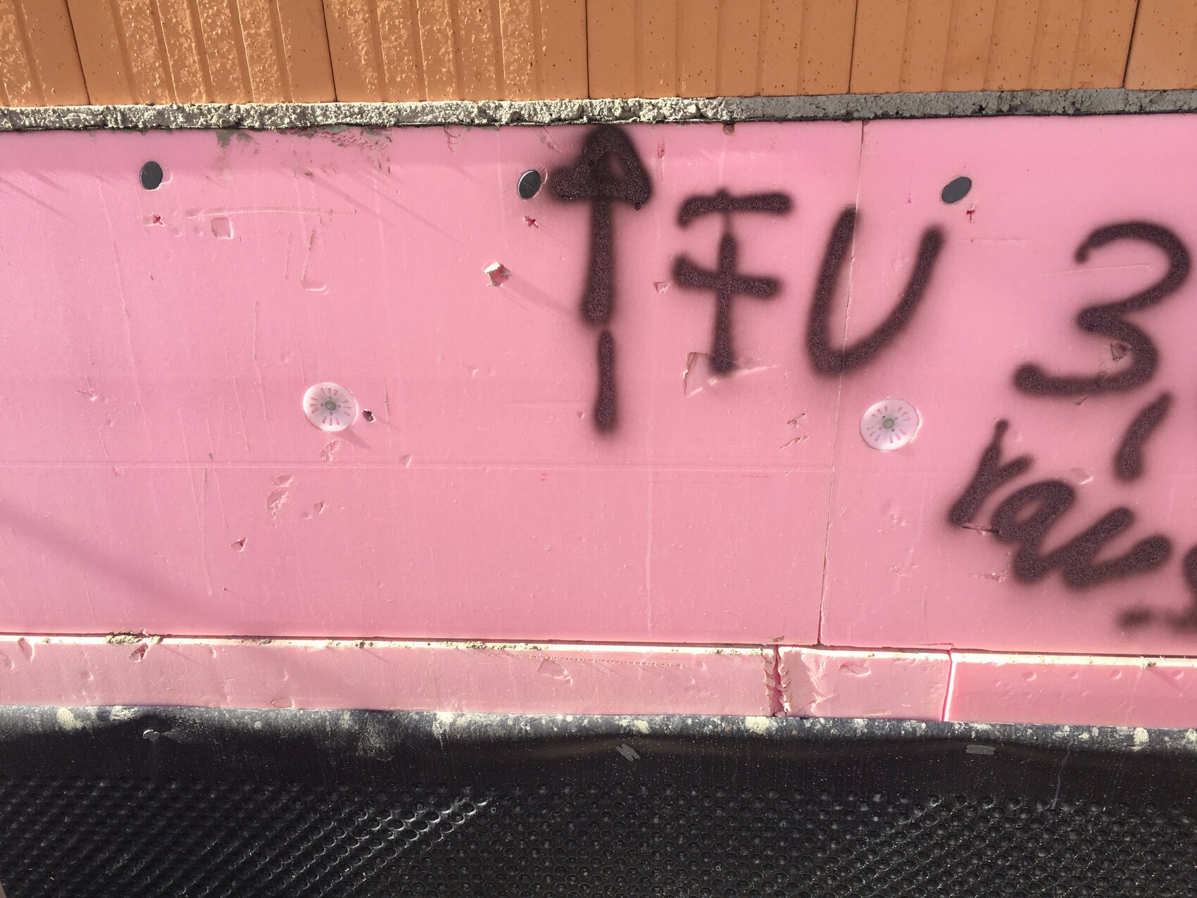 Pinkfarbene Dämmplatten aus Polyurethan an einer Wand einer Baustelle, Graffiti sichtbar