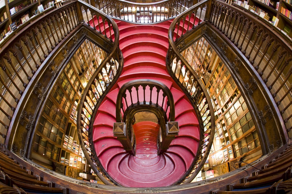 Spiralförmige rote Treppe in einer Bibliothek, umgeben von Bücherregalen und Holzgeländern.