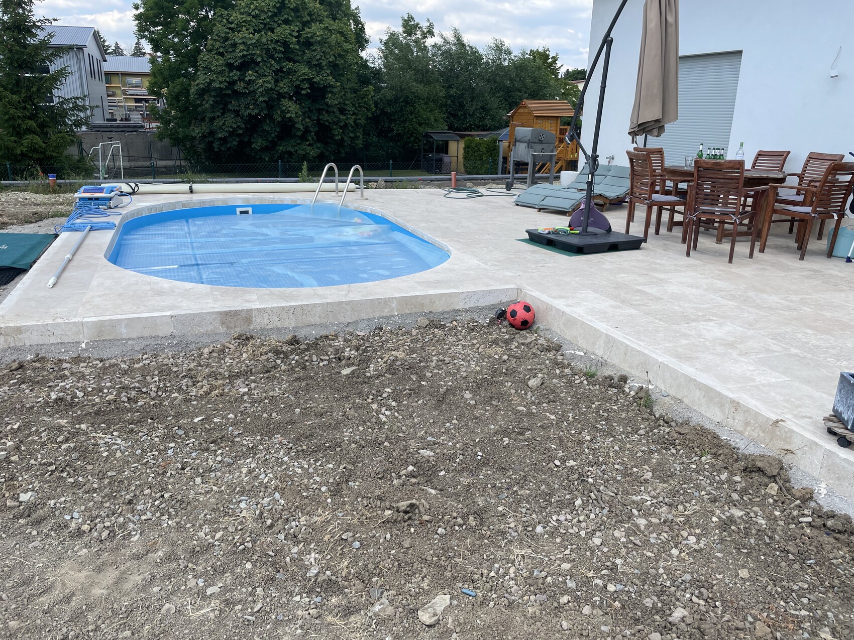 Garten mit ovalem Pool, Terrasse mit Tischgruppe und Sonnenschirm; roter Ball am Rand.