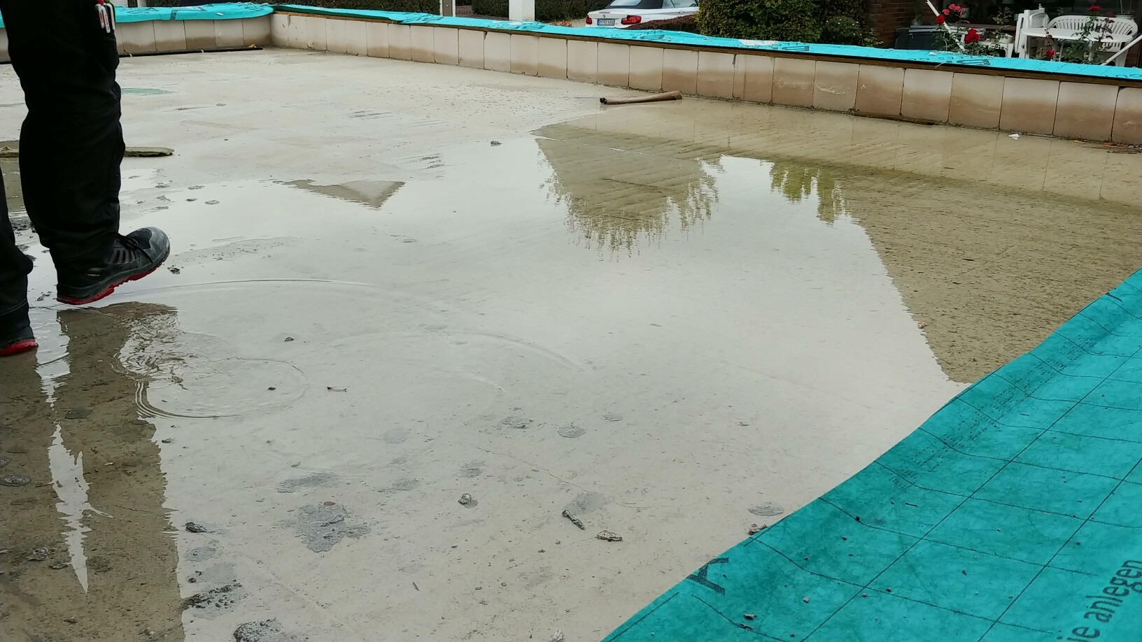 Nasser Betonboden am Poolfundament, Bauarbeiter steht am Beckenrand.