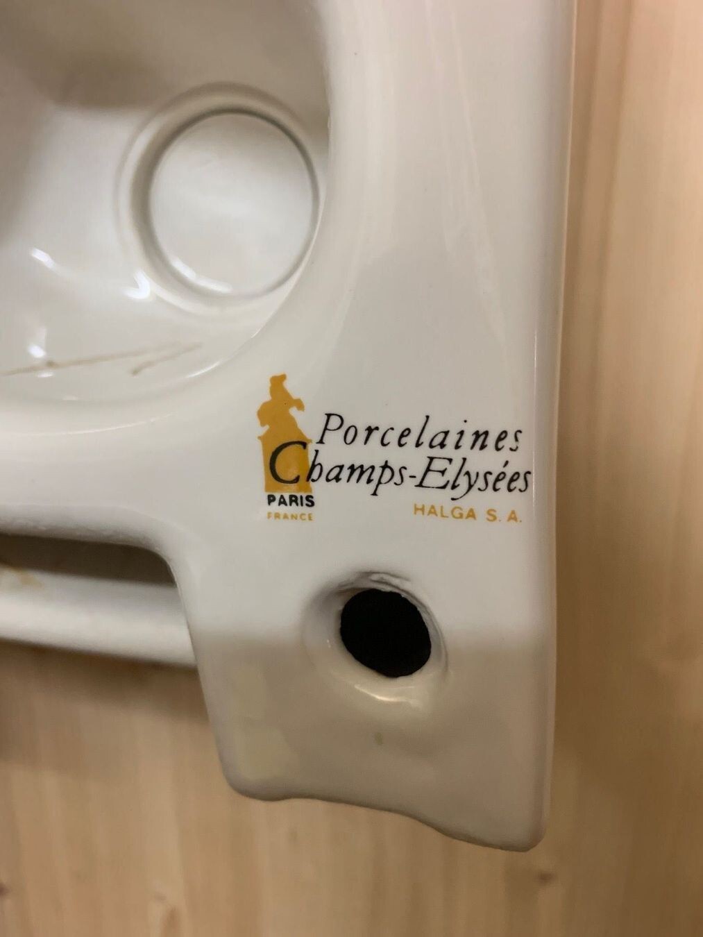 Weiße Porzellanplatte mit Logo „Porcelaines Champs-Elysées“ und runder Lochöffnung.