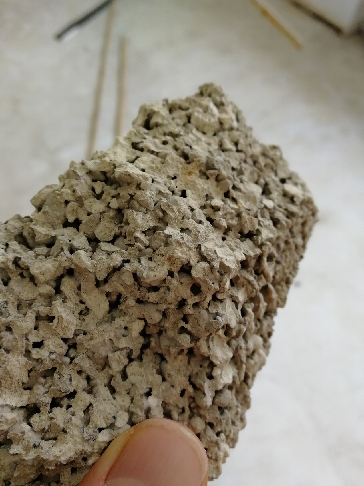 Poröses braun-graues Gestein mit vielen Hohlräumen, von einer Hand gehalten.