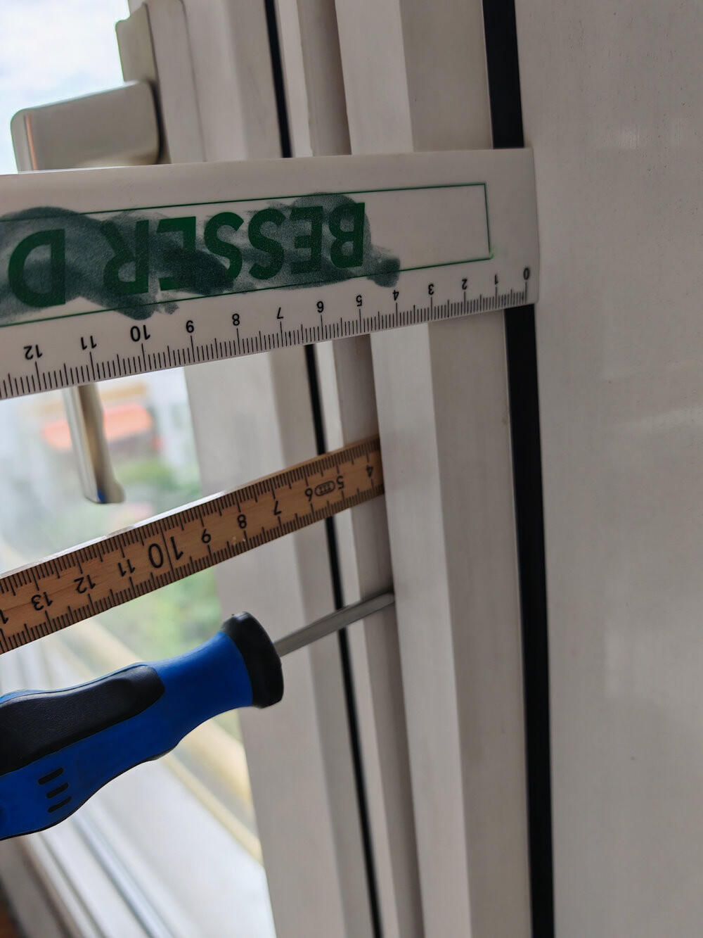 Nahaufnahme eines Fensterrahmens mit Maßband (Zoll) und Schraubendreher.