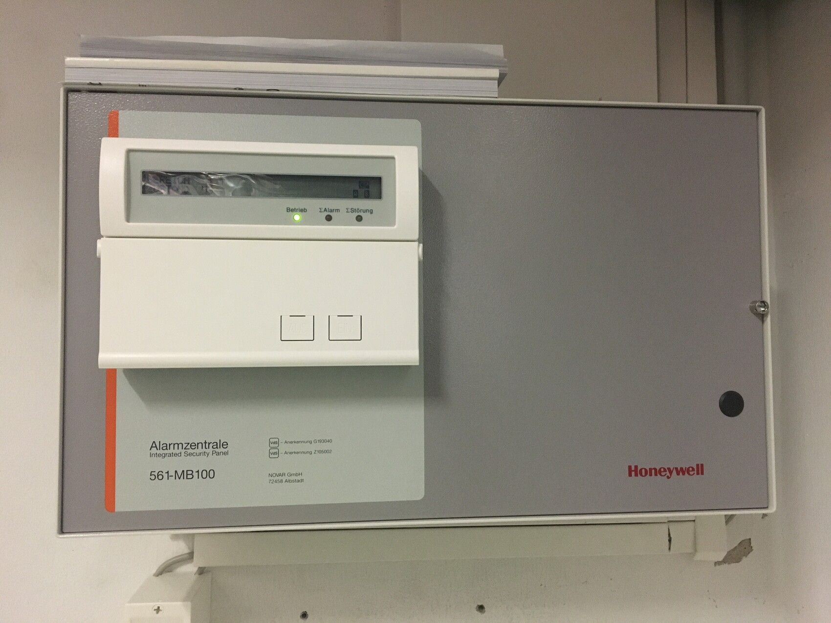 Alarmzentrale Honeywell mit Display, zwei Knöpfen und grünem Statuslicht, an der Wand montiert.