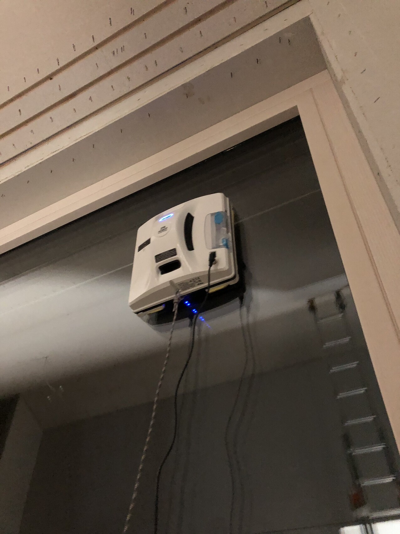 Weißer Deckenprojektor über dem Türrahmen, Kabel hängen herab, graue Wände.