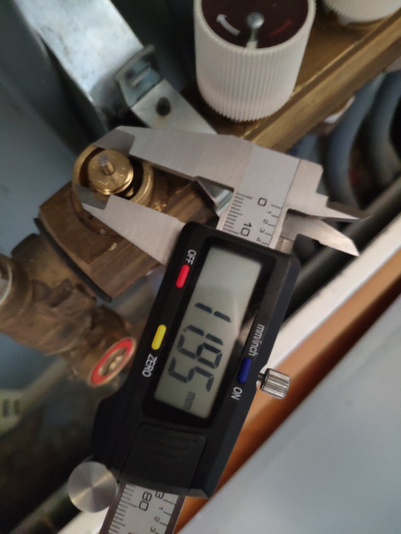 Nahaufnahme eines digitalen Messschiebers, der eine goldfarbene Schraubverbindung zwischen Metallteilen misst.
