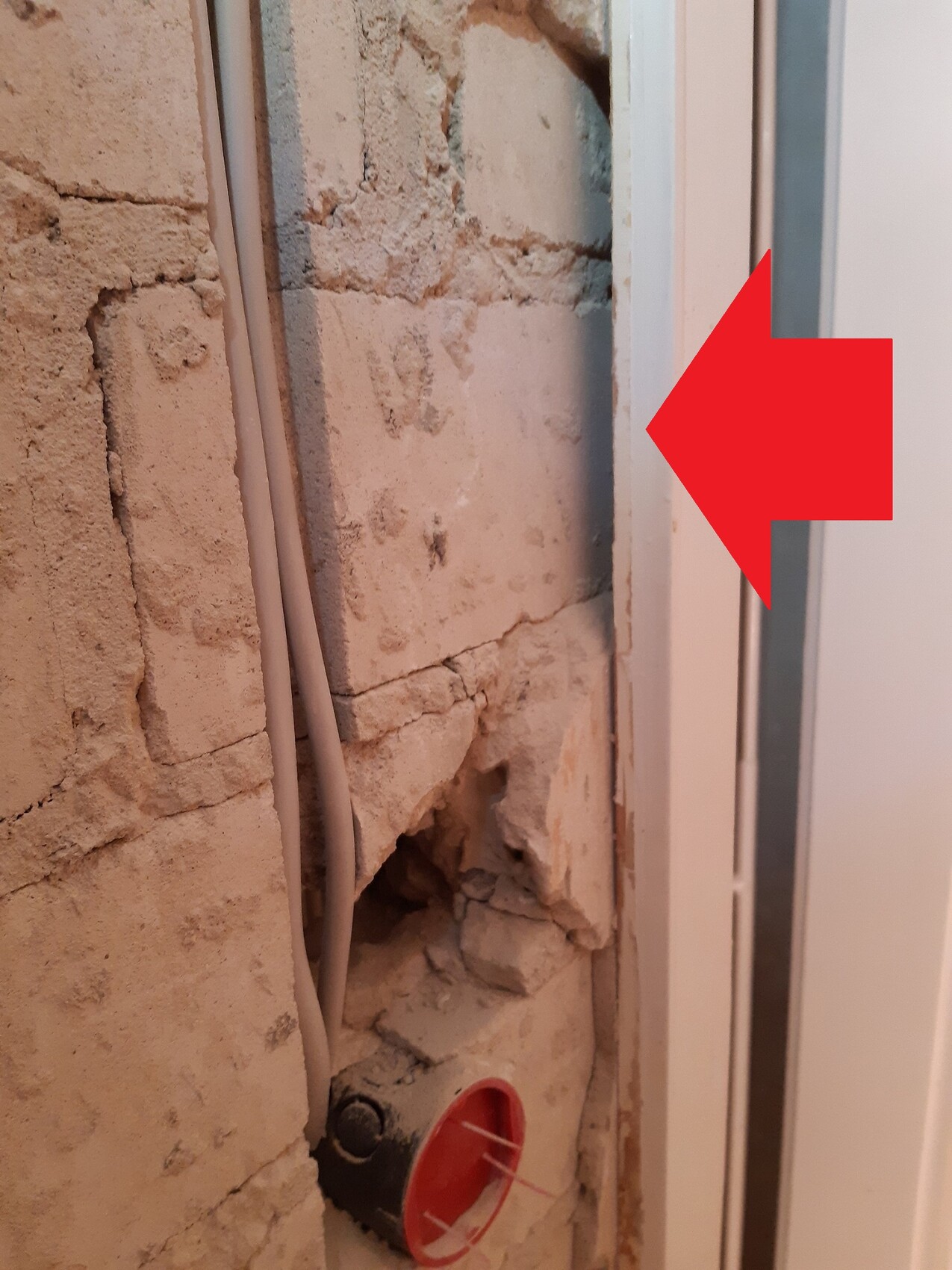 Offene Ziegel- bzw. Putzwand neben Türrahmen, sichtbare Kabelleitung und roter Abdeckkappe am Boden.