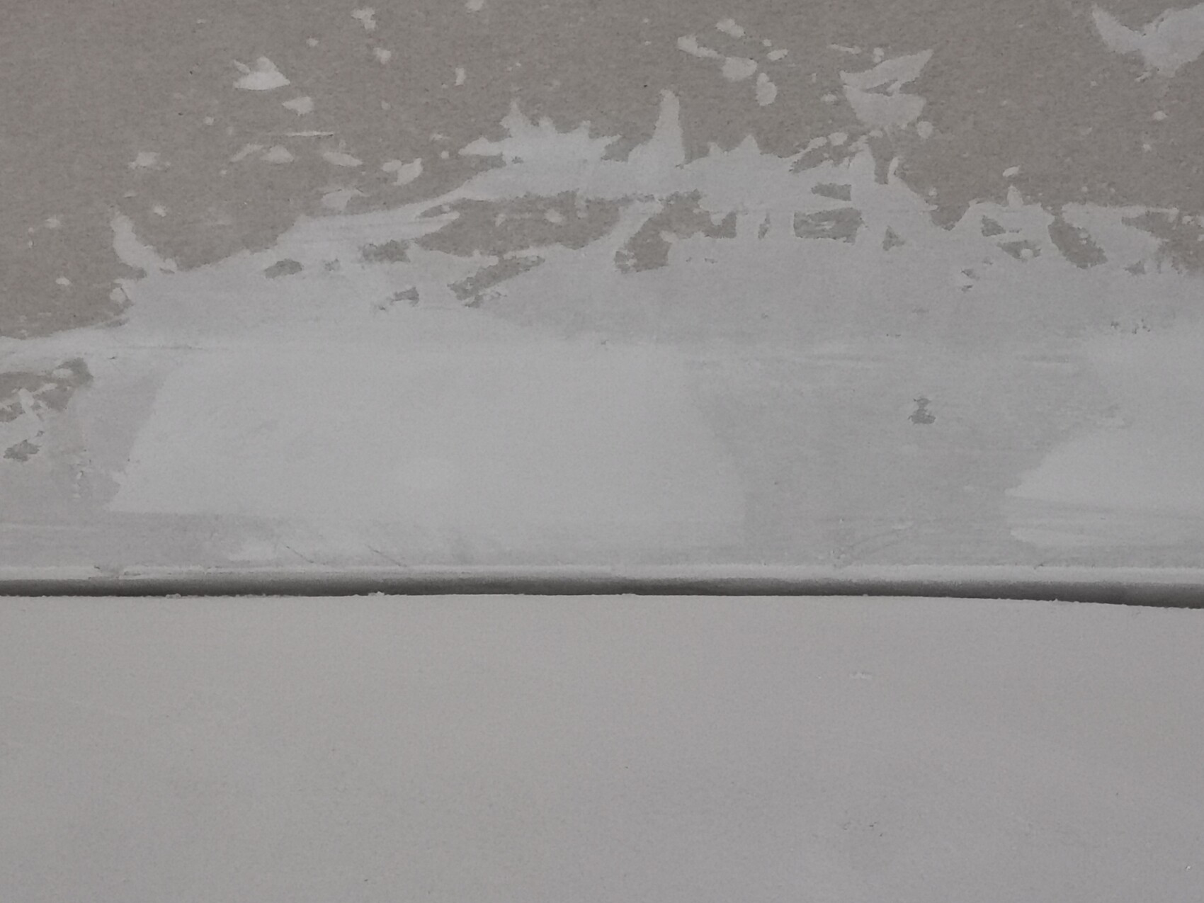 Nahaufnahme einer Wand mit abgeblättertem Putz und Rissen an der unteren Kante.