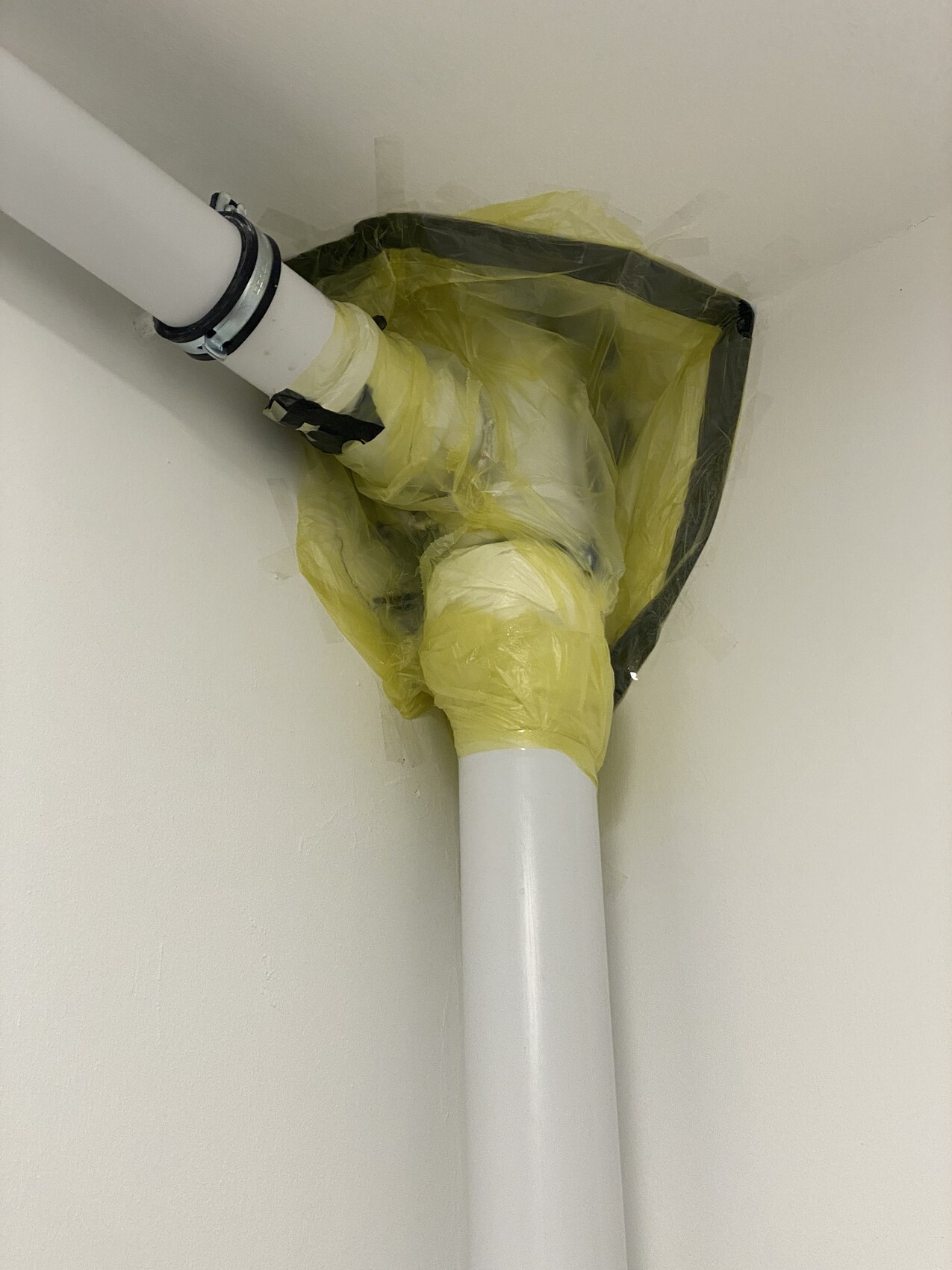 Weißes PVC-Rohr in Ecke, gelbe Folie um eine Rohrverbindung gewickelt.