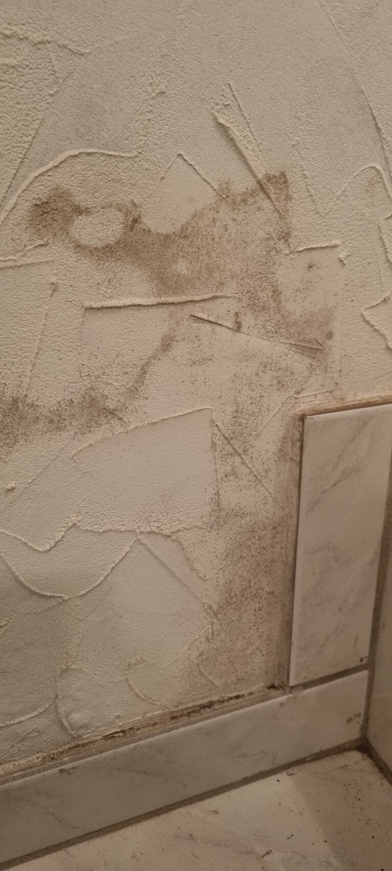 Wand mit rauer, unregelmäßigem Putz, Flecken und Linien; Boden aus Fliesen unten.