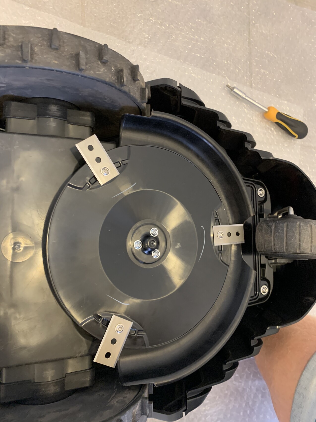 Rundes schwarzes Gehäuse mit drei Metallhalterungen um zentrale Schraube, Teil eines Geräts.