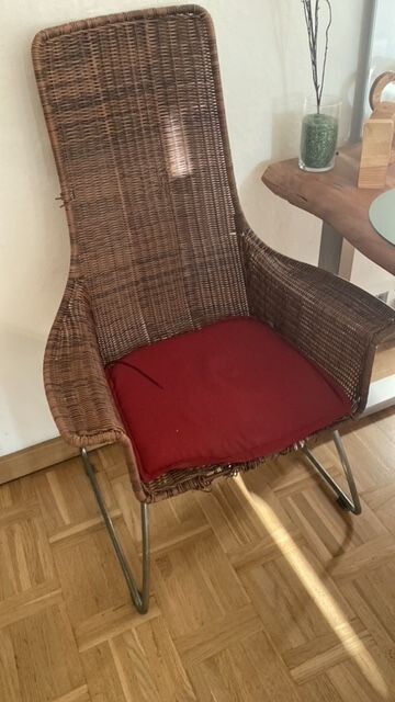 Geflochtener Sessel mit rotem Kissen im Wohnzimmer neben Tisch mit Deko.