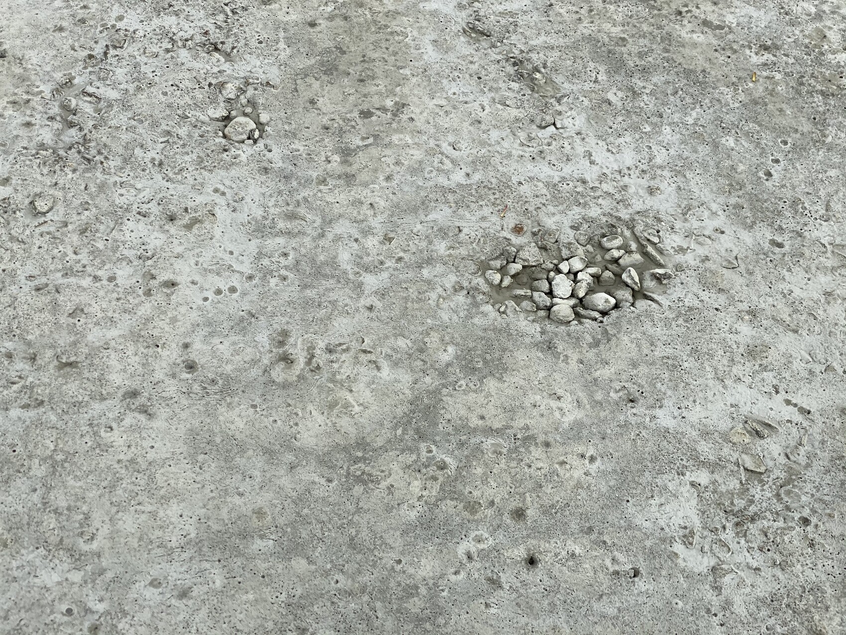Grauer Betonboden mit einer kleinen Ansammlung Kieselsteine rechts der Mitte.