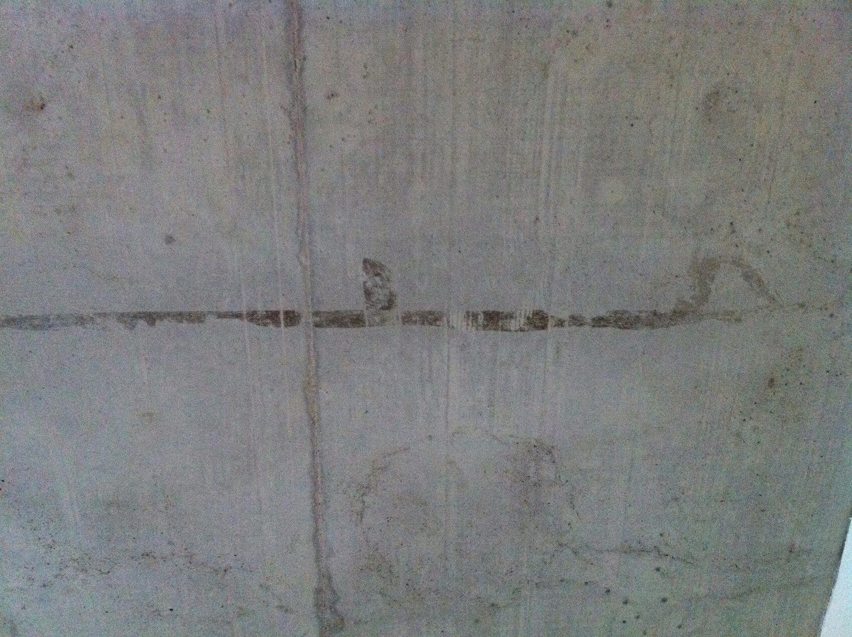 Betonwand mit horizontaler, dunkler Linie und sichtbaren Rissen.