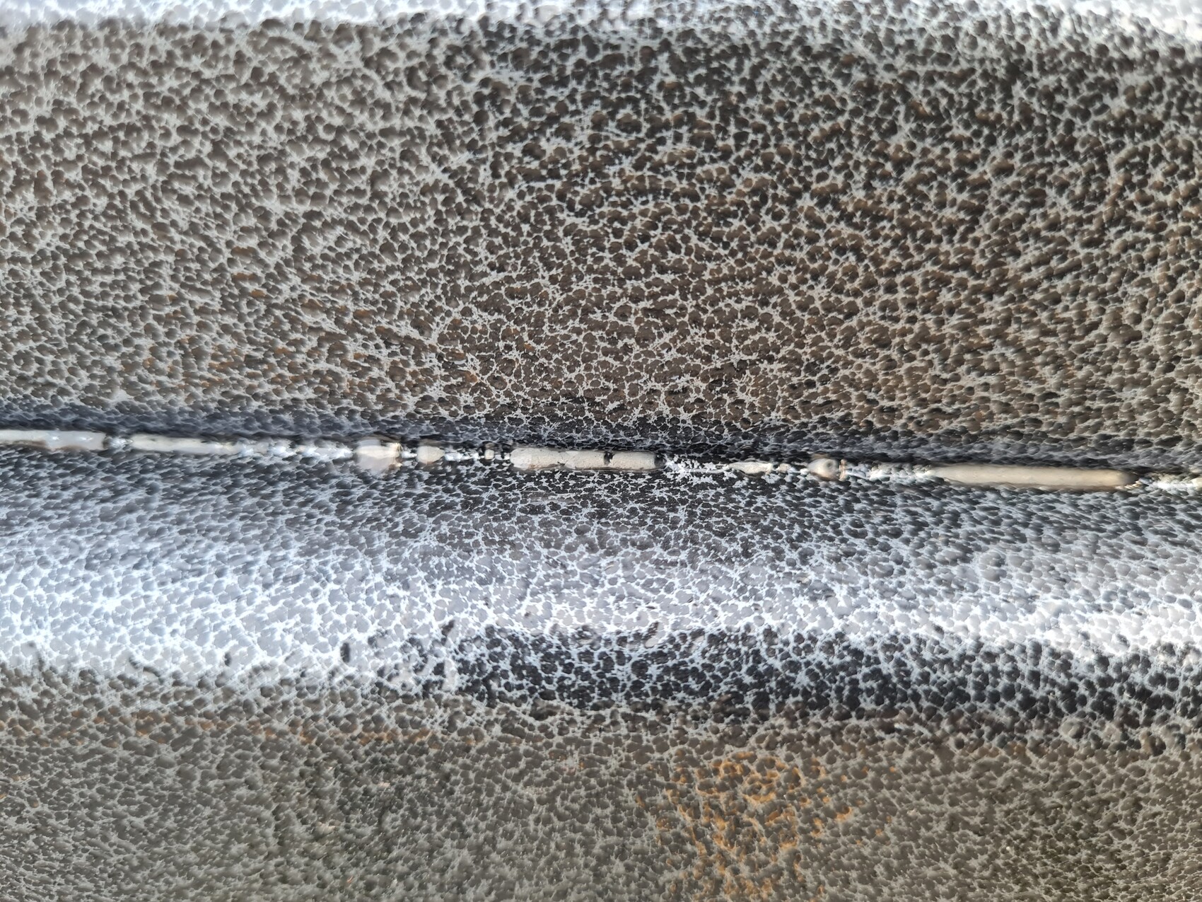 Nahaufnahme einer rauen, geprägten Metalloberfläche mit einer horizontalen Naht.