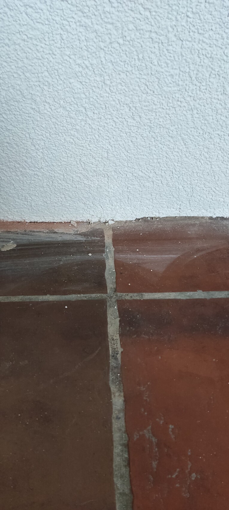 Weiße grobe Wand über braunen Fliesen mit grauen Fugen und Staub.