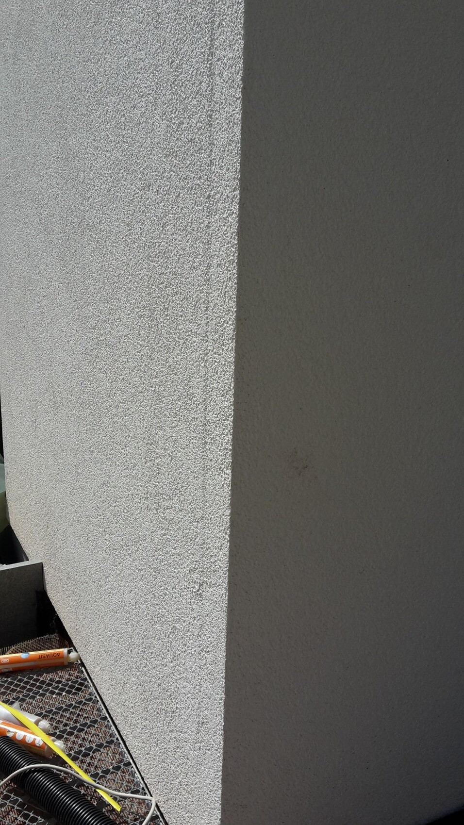 Außenwand-Ecke: helle linke Putzfläche neben dunkler rechter Wand; Baustellenzubehör unten.