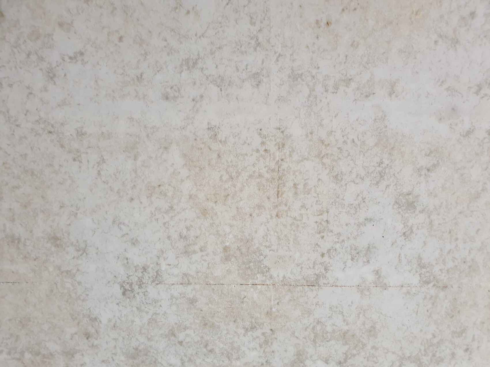 Abgenutzte weiße Wand mit unregelmäßigen, beige-hellen Flecken und Textur.