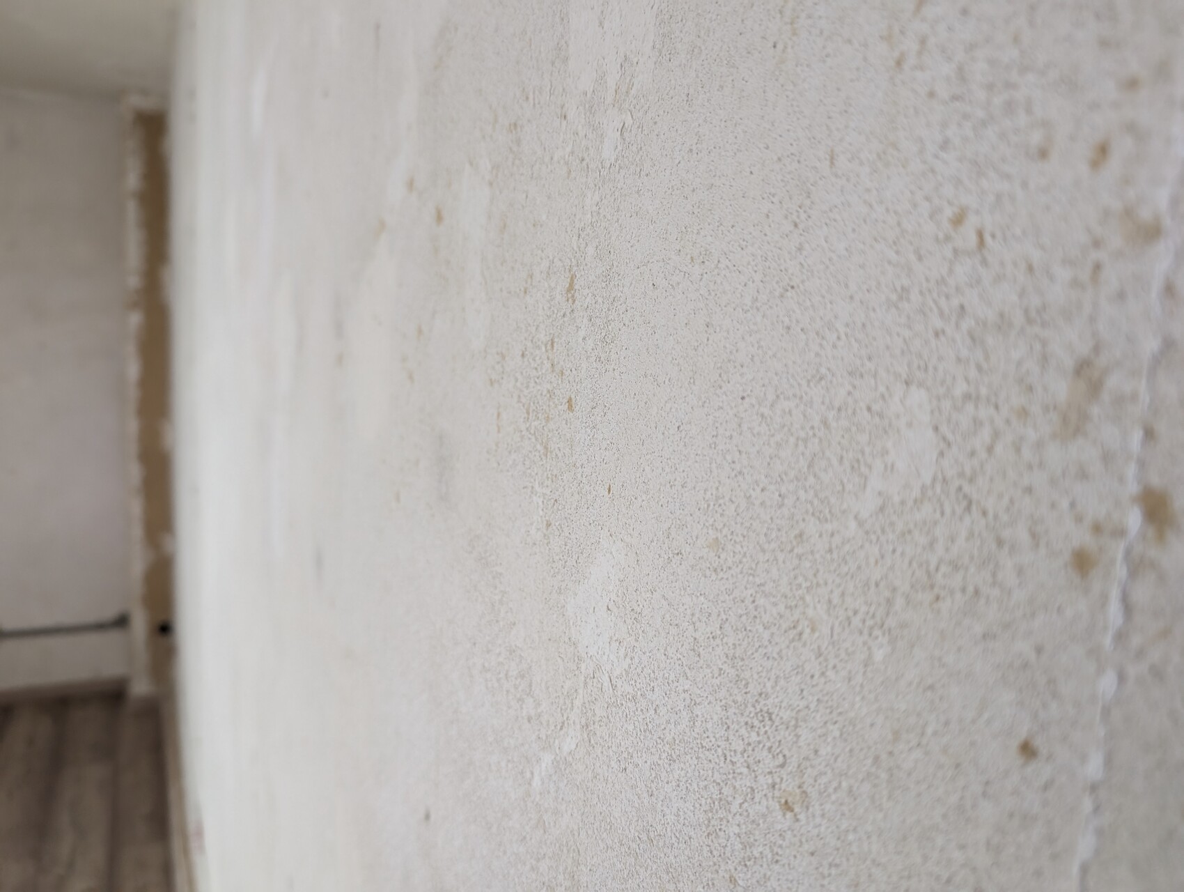 Nahaufnahme einer verputzten Wand mit unregelmäßigen Flecken; linke Kante sichtbar.