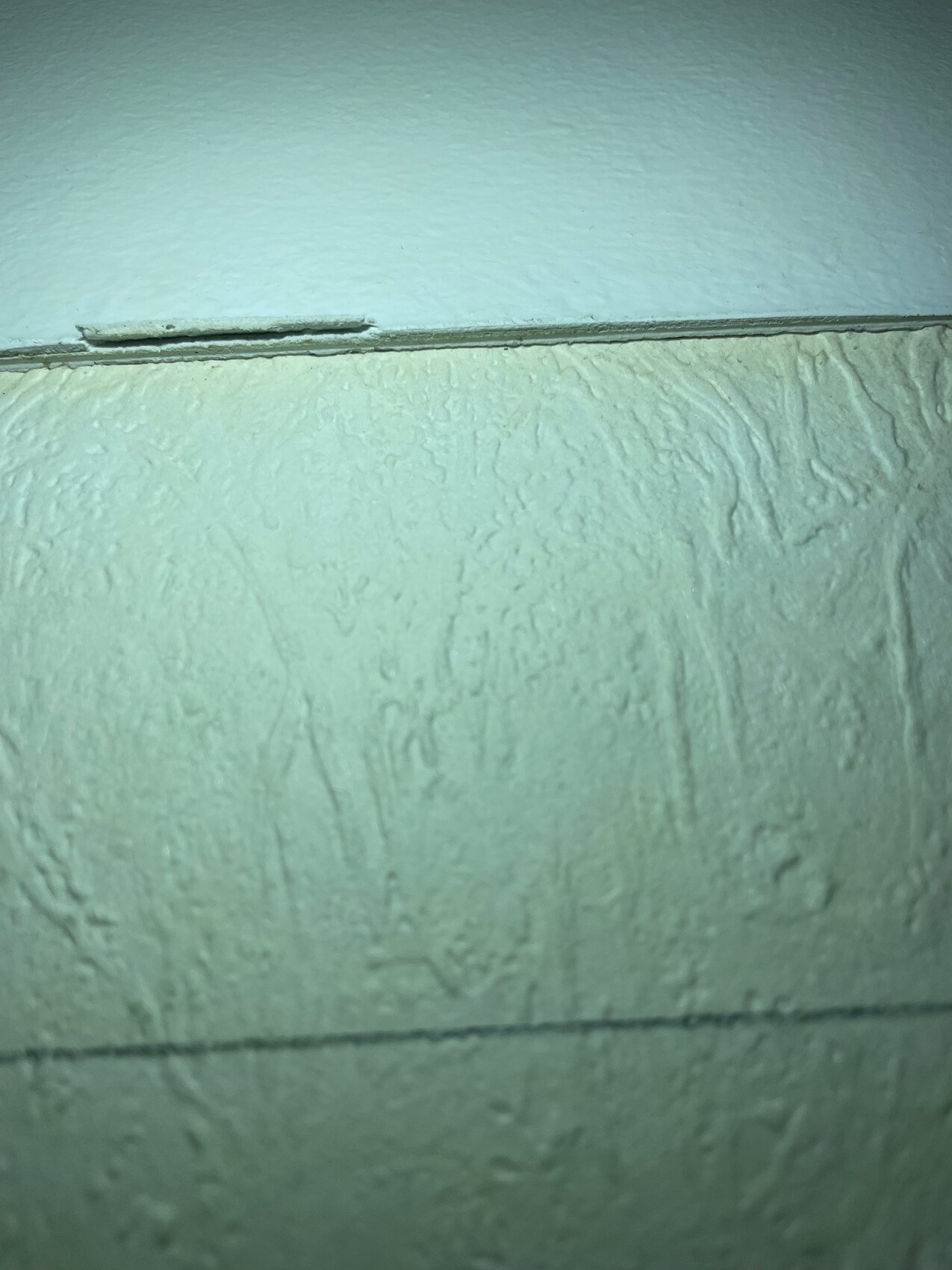 Nahaufnahme einer rauen, texturierten Wand mit einer dünnen Leiste am oberen Rand.