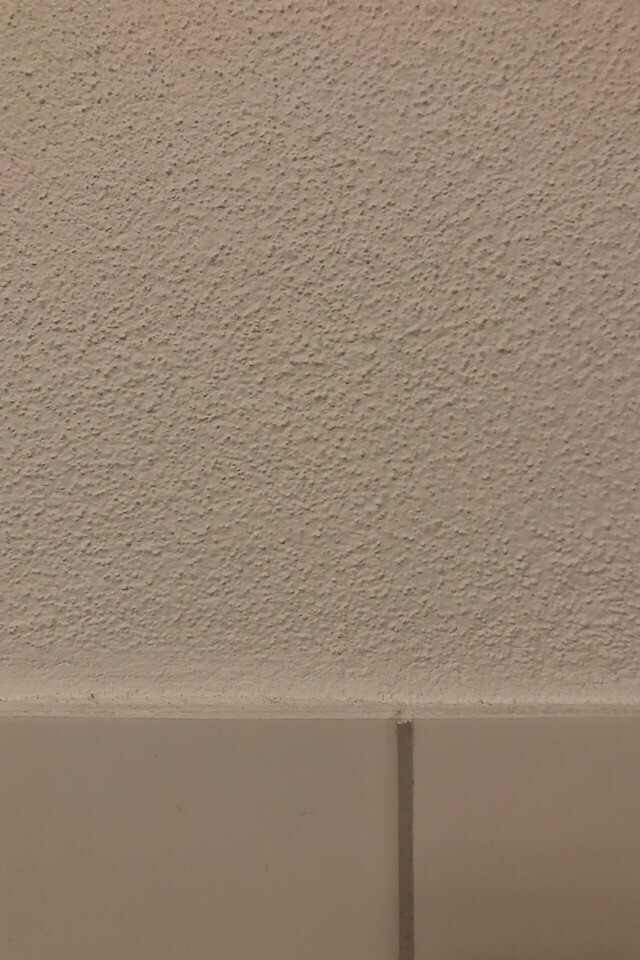 Texturierte grob verputzte Innenwand in hellbeige mit unterem Fliesenbereich.