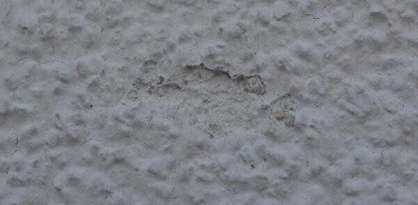 Nahaufnahme einer rauen verputzten Wand mit Putzschäden und Unebenheiten.