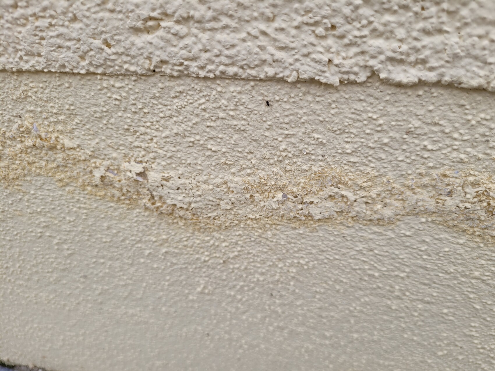 Nahaufnahme einer rauen, cremefarbenen Wand mit abblätterndem Putz.