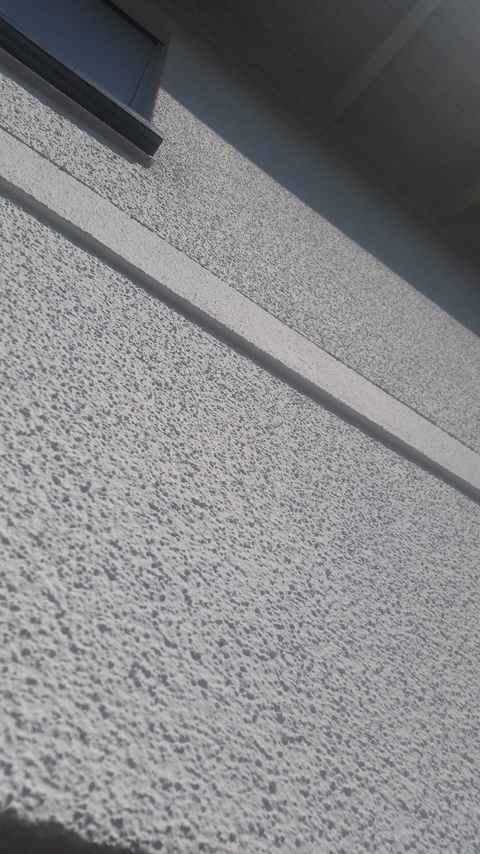 Aussenwand mit rauer Putzstruktur und kleinem Fenster.