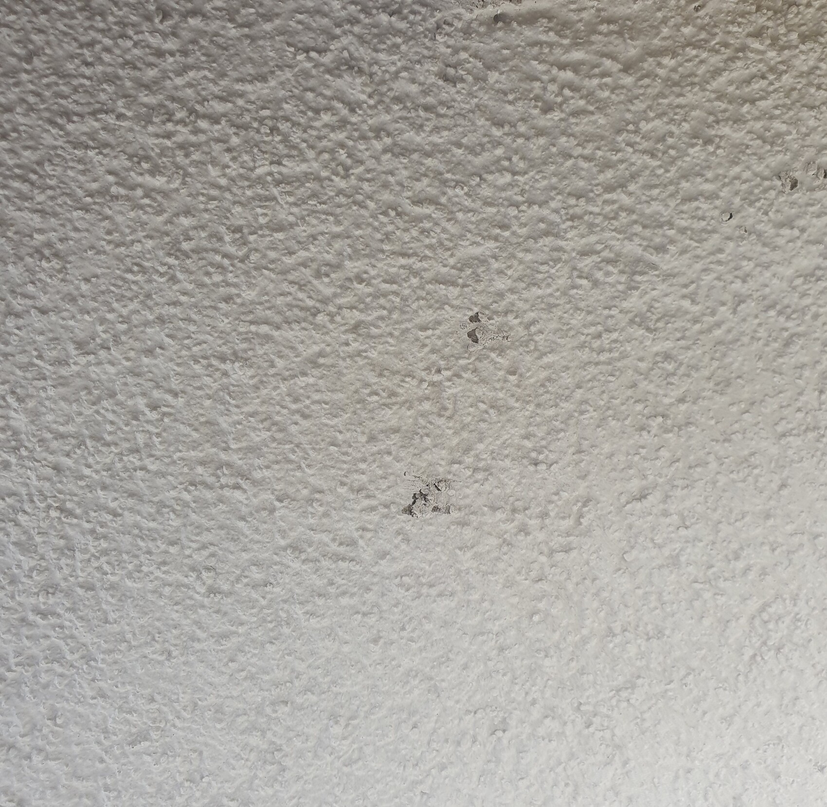Weiße, grob texturierte Wand mit zwei kleinen dunklen Flecken.