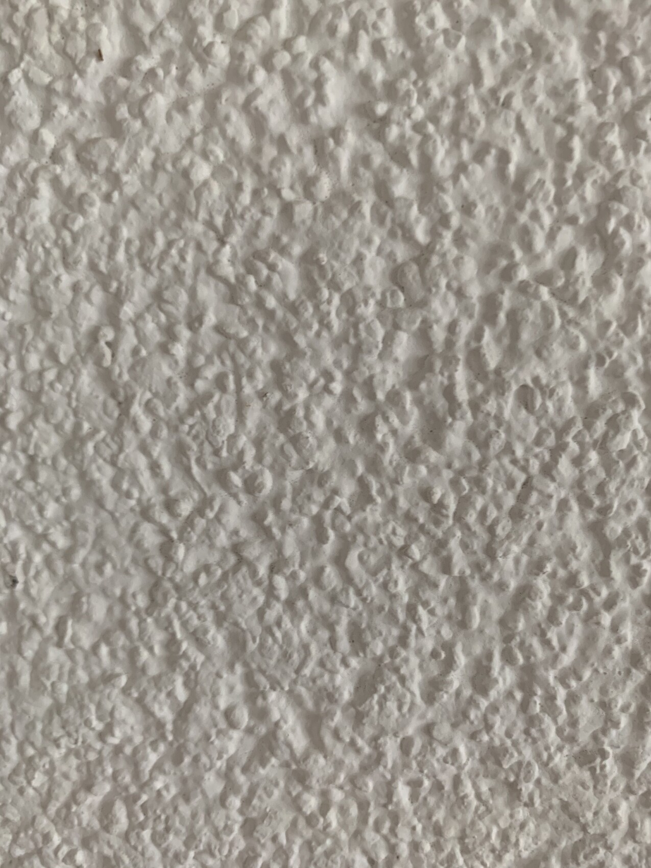 Weiße Wand mit grober, unregelmäßiger Putzstruktur und kleinen Vertiefungen.
