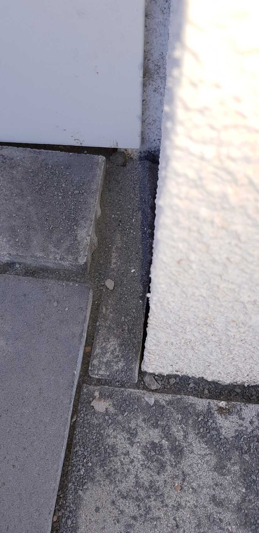 Nahaufnahme einer grauen Stein-Stufe neben einer weißen Türverkleidung und rauer Wand.