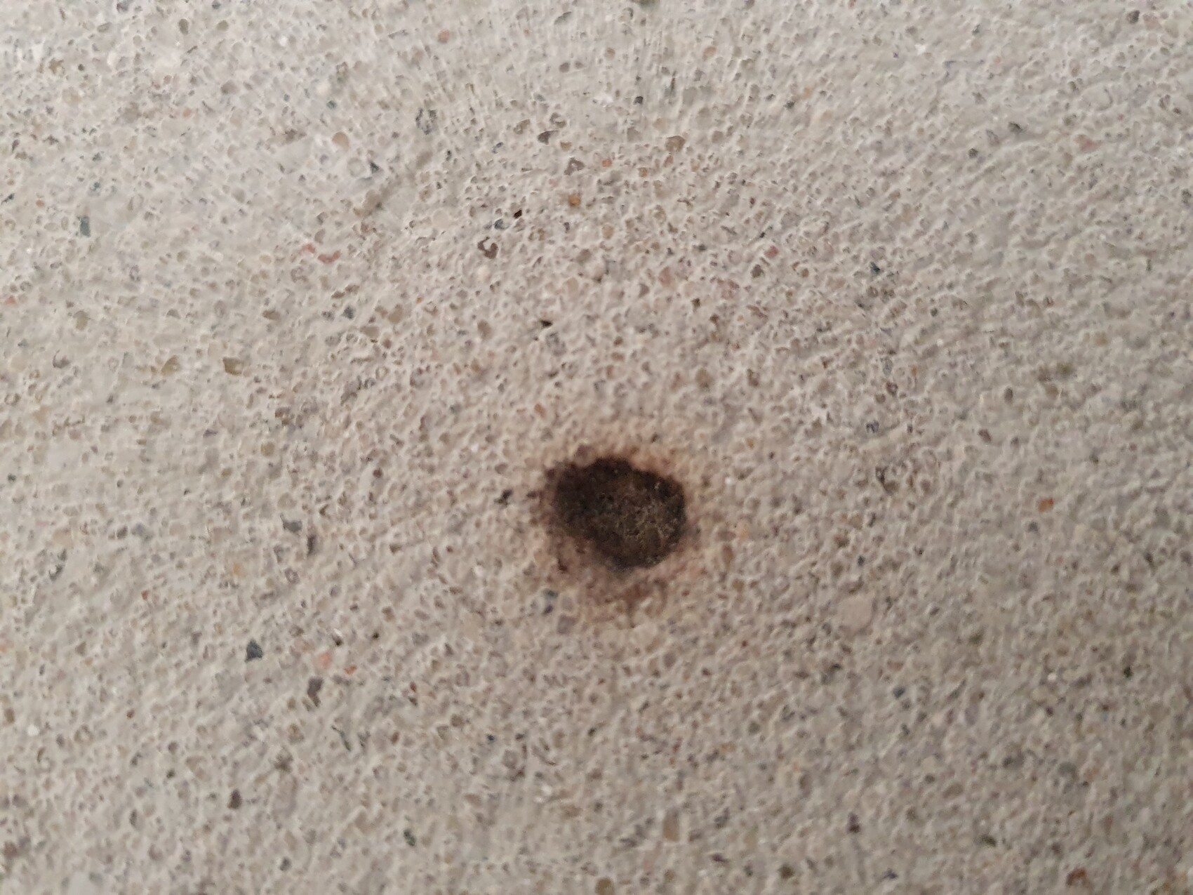 Kleine dunkle runde Vertiefung in einer rauen Betonoberfläche.