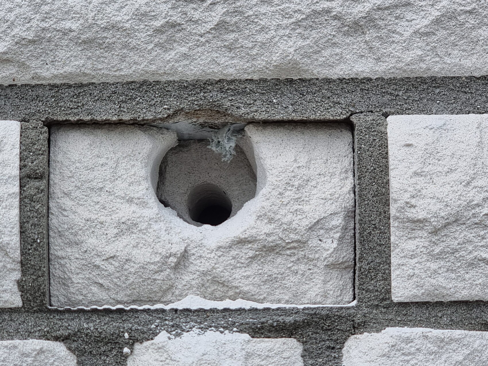 Nahaufnahme eines Betonblocks mit rundem Loch und rauer Steinoberfläche.