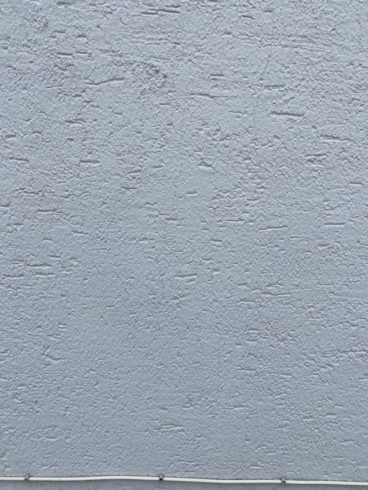 Grau verputzte Wand mit rauer Struktur; unten sichtbare weiße Leitung.
